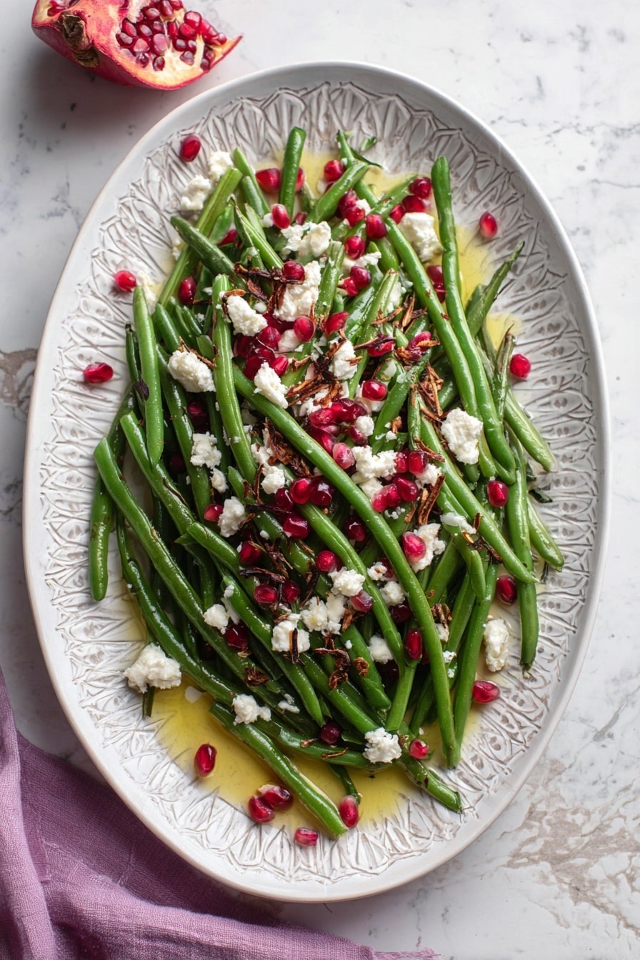 The dish is served on a white plate with a subtle grey pattern, placed on a white marbled surface. The base layer is a pile of bright green beans, fresh and slightly glossy, arranged in a loose mound. Scattered on top are vivid red pomegranate seeds, adding bright, jewel-like spots over the green beans. White crumbles of soft cheese are spread evenly across the dish, providing a creamy contrast. Small pieces of browned, crispy bits are sprinkled sparingly over the entire salad, adding texture and depth. The whole dish is lightly drizzled with golden olive oil, visible around the edges, enhancing the colors and giving a slight shine. photo taken with an iphone --ar 2:3 --v 7 - Maple Mustard Green Beans with Pomegranate and Goat Cheese, healthy green bean side dish, spring green beans recipe, fruit and cheese salad, easy vegetable side dish